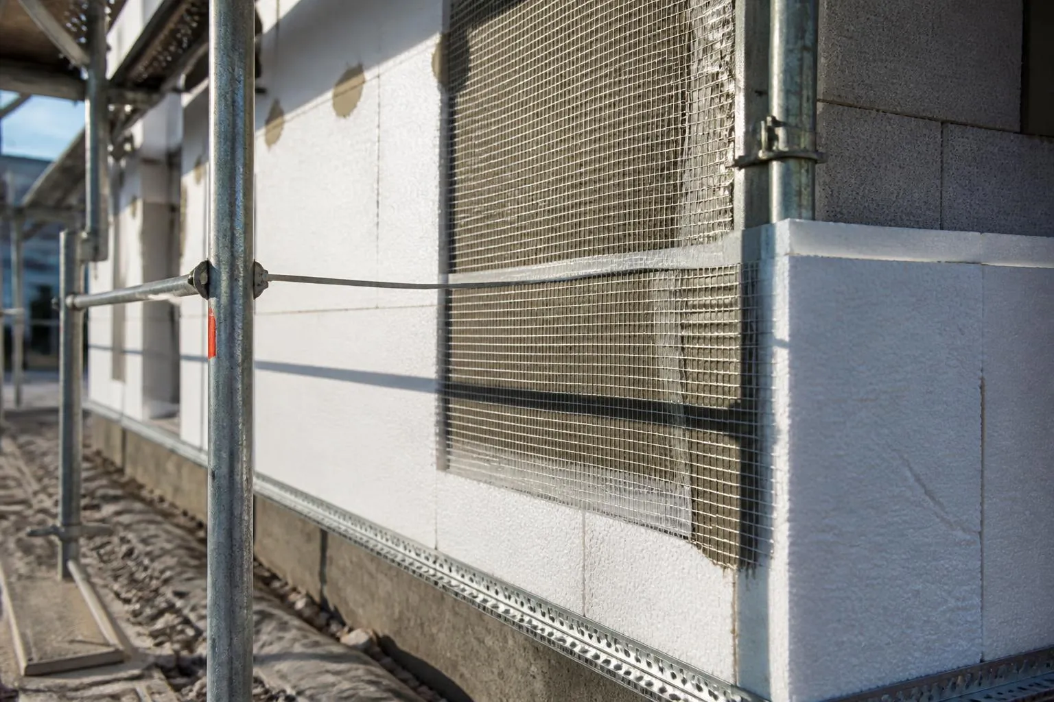 Panneaux de polystyrène blanc collés sur un mur de façade, posés sur un rail de départ en aluminium.